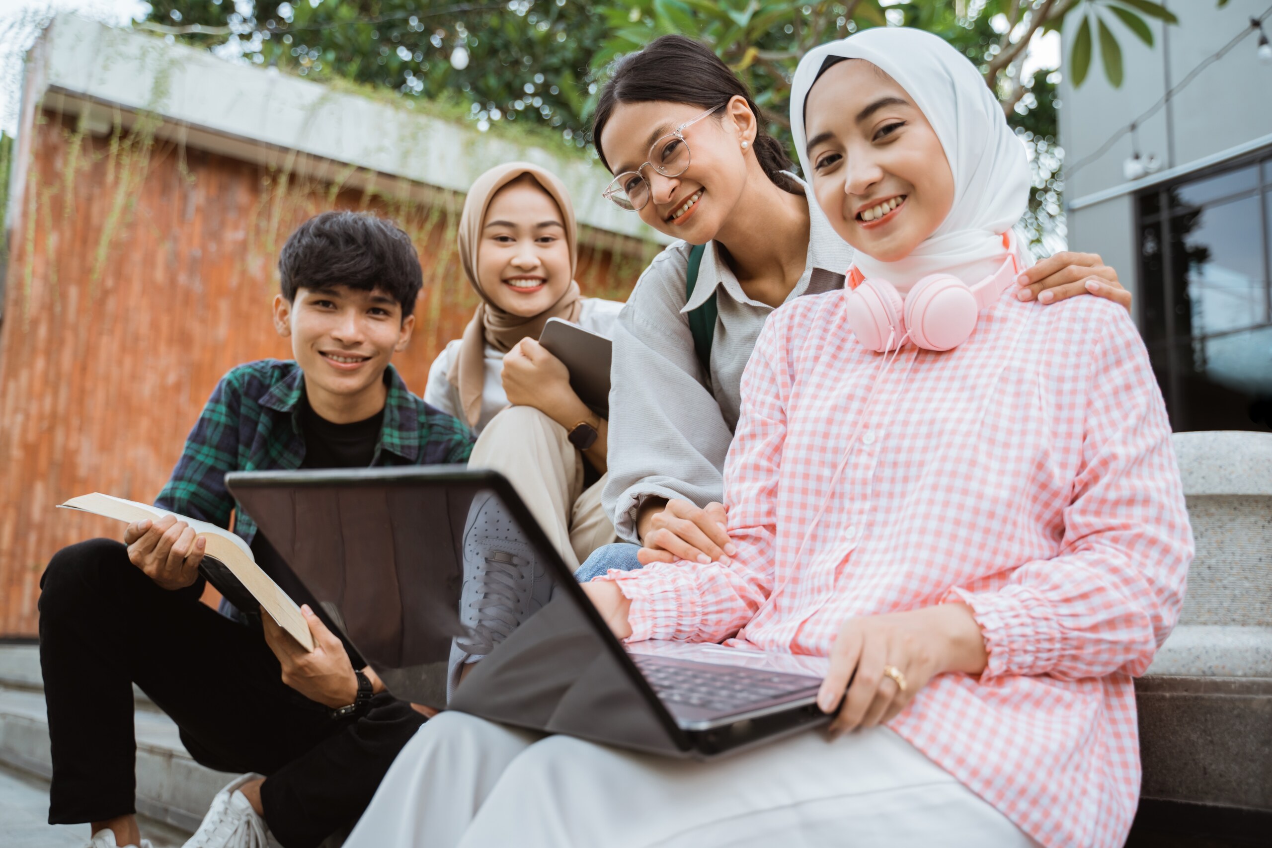 Quatre étudiants assis ensemble en plein air avec des livres et des tablettes