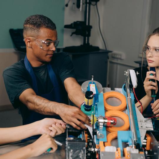Group of young female and male apprentices working at table with tools.