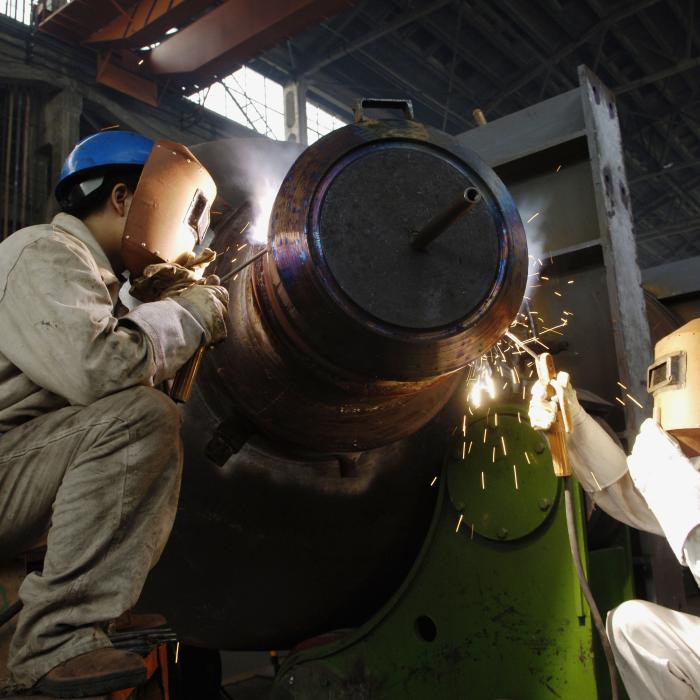 Two men welding, wearing protective face covering and suits.
