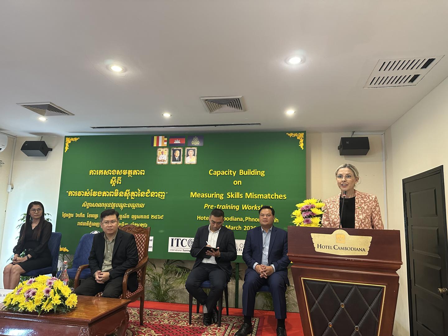 Woman standing at a podium and a panel sitting behind her