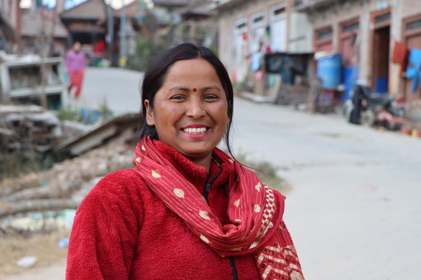 A woman wearing red clothing smiling in a neighbourhood in Nepal