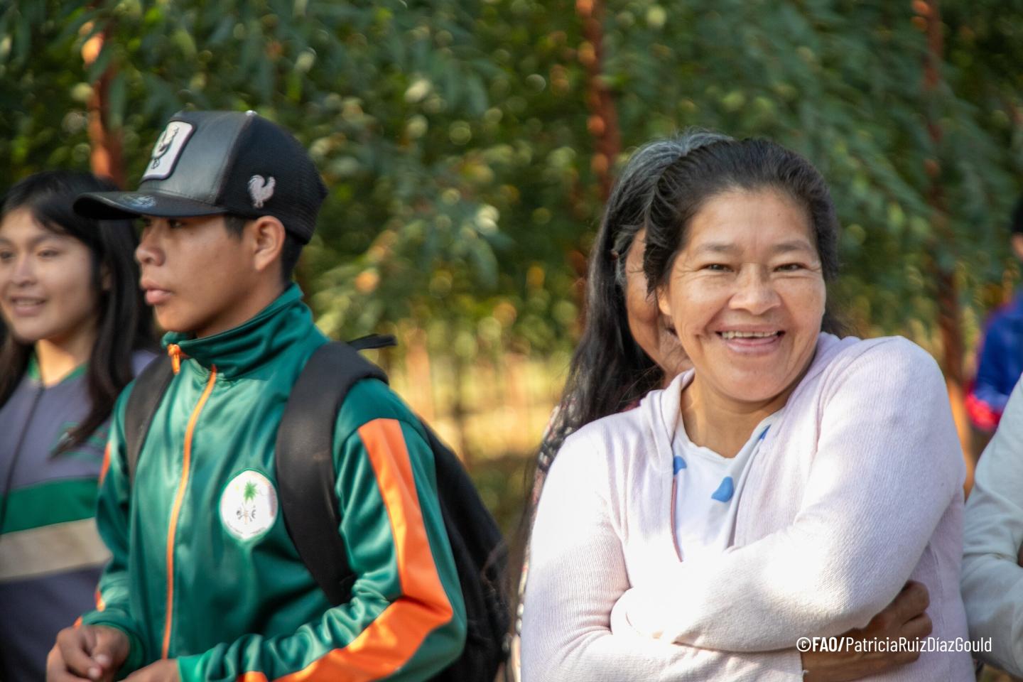A smiling woman seated outdoors beside young people in green sportswear